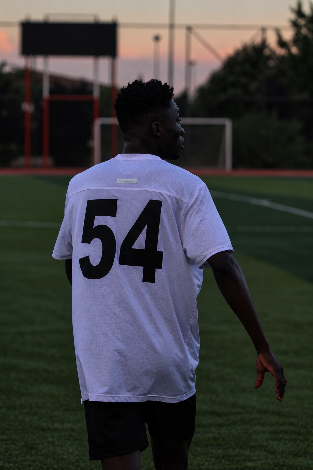 Footballer wearing number 54 on the pitch at dusk, seen from behind